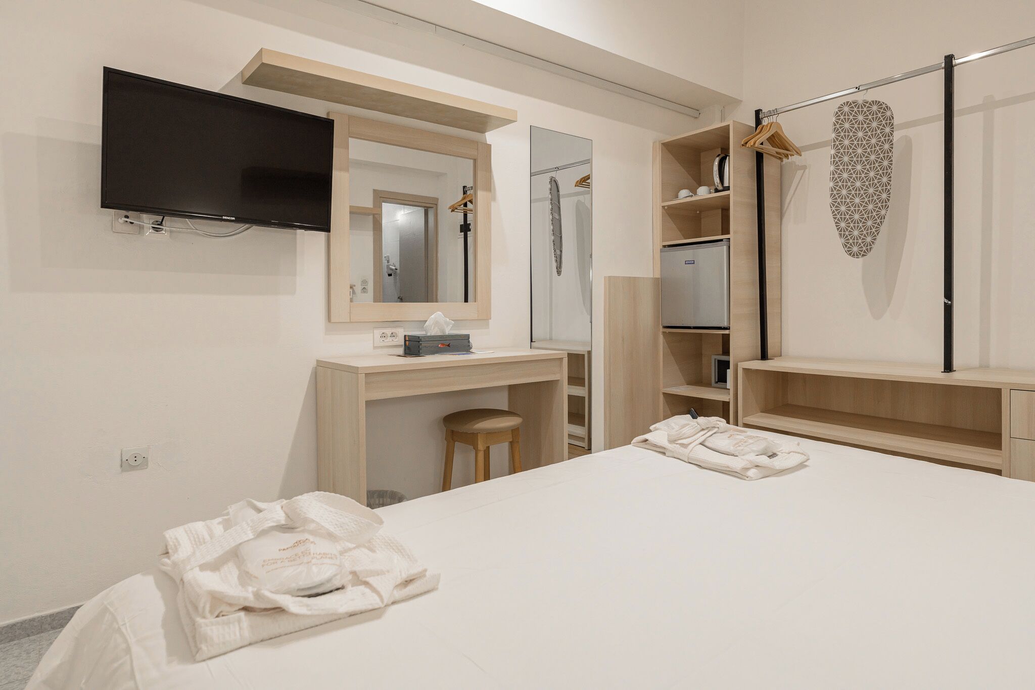 A hotel room with a bed, a desk, a mirror, a television, and a wardrobe.