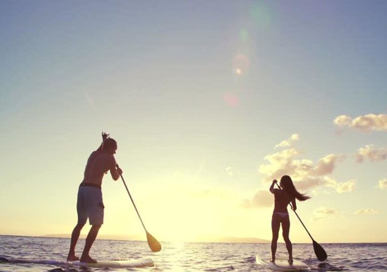 Two people paddleboarding on a beach at sunset.