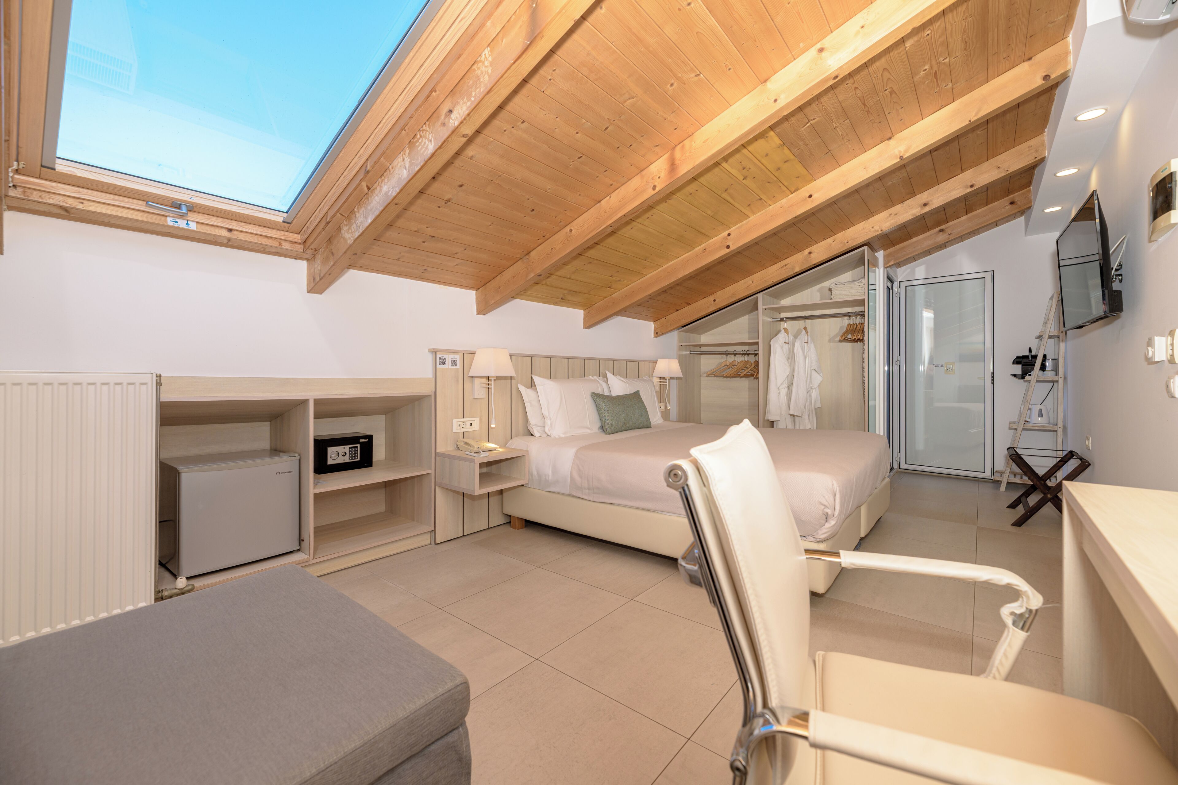 A bedroom with a skylight, a bed, a desk, a chair, a radiator, and a wardrobe.
