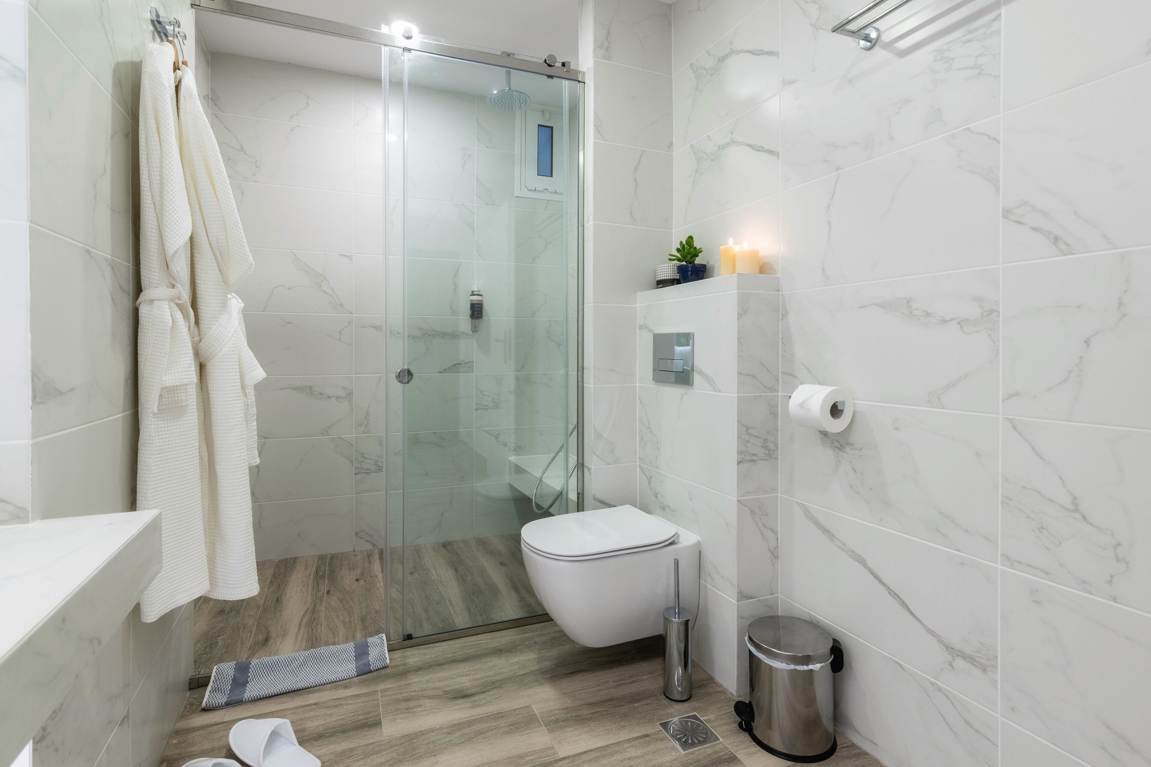 A modern bathroom with a glass-enclosed shower, a toilet, a bidet, and a trash bin.
