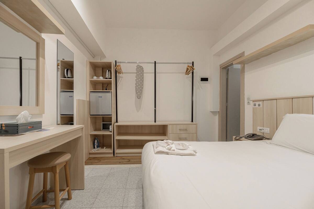 A modern hotel room with a wooden desk, a large mirror, a wardrobe, and a bed with neatly folded towels.