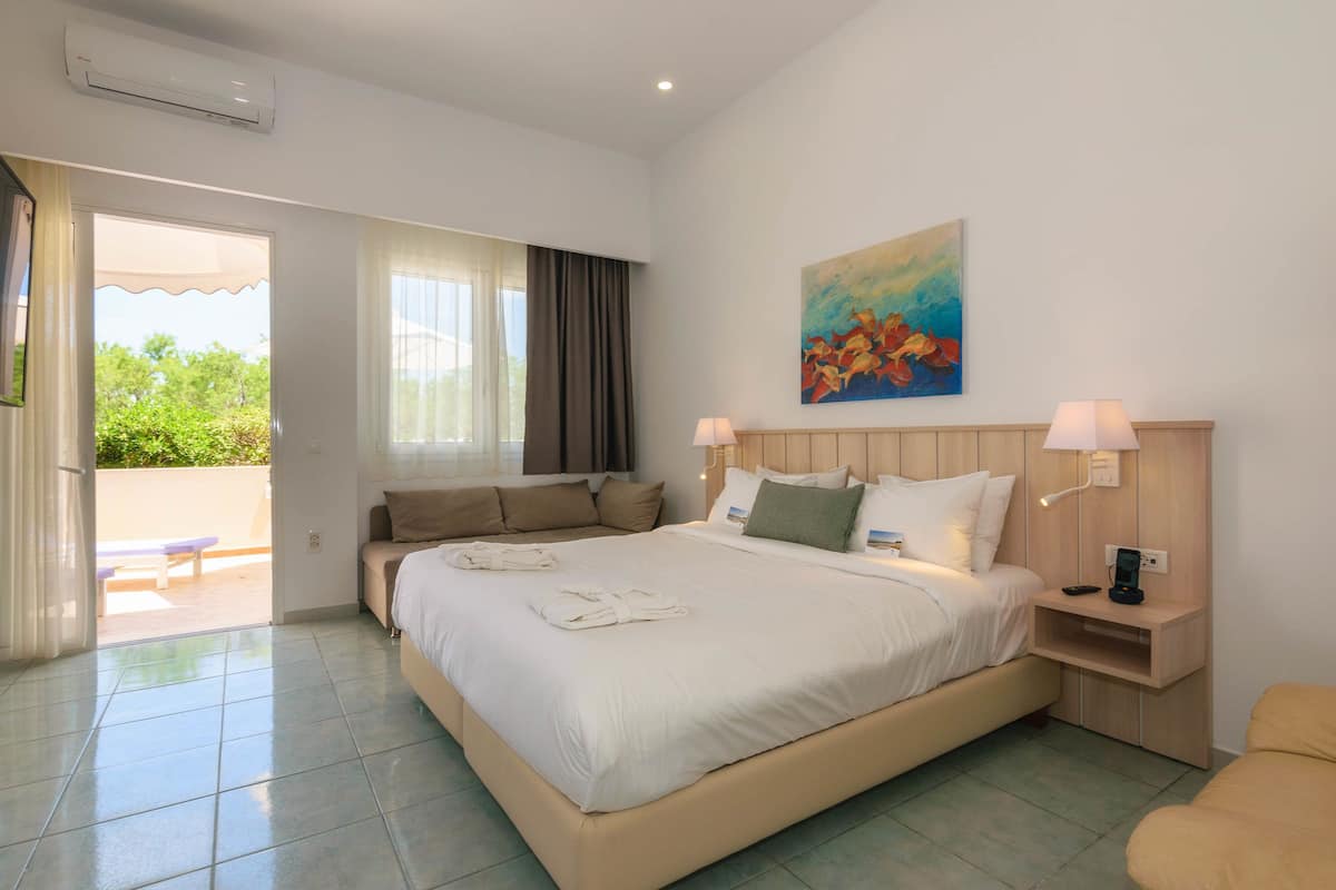 A hotel room with a large bed, a sofa, a desk with a lamp, and a painting on the wall.