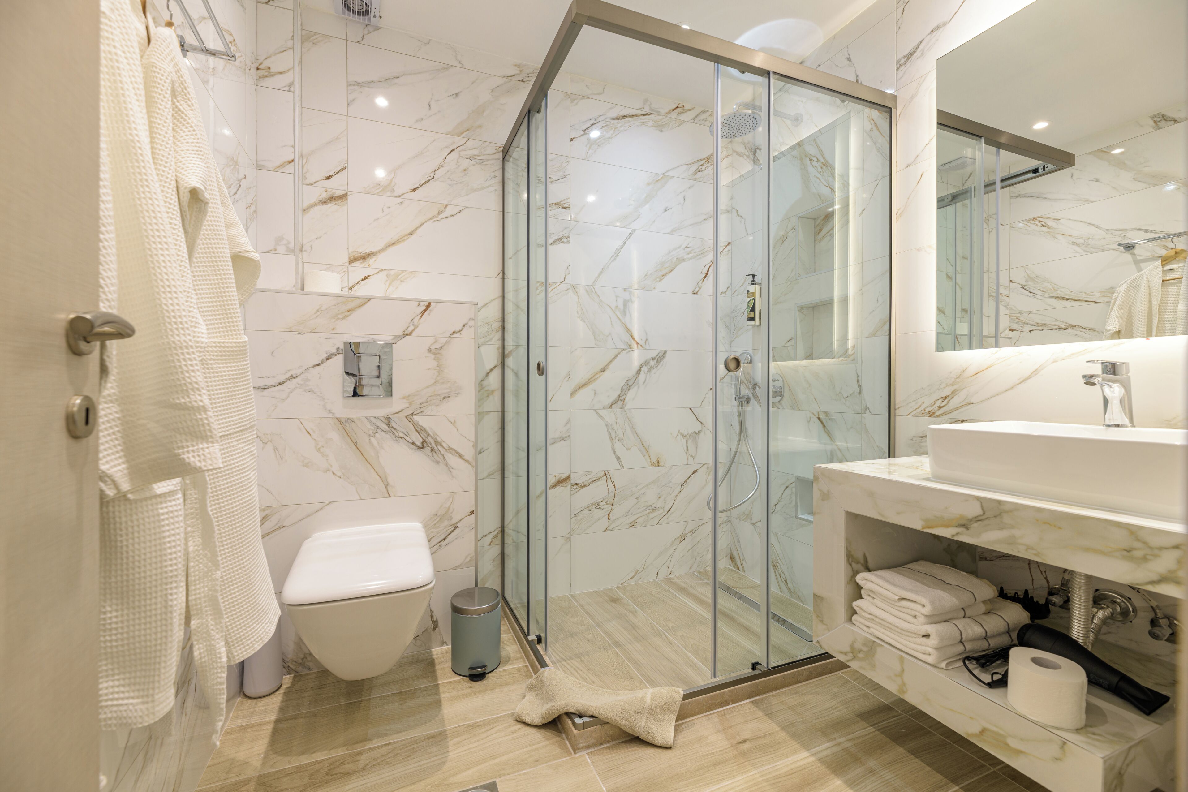 A modern bathroom with a glass shower enclosure, a toilet, a sink with a marble countertop, and a mirror.