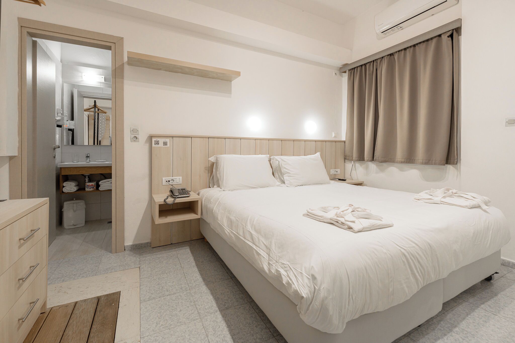 A hotel room with a bed, bedside table, and a mirror.