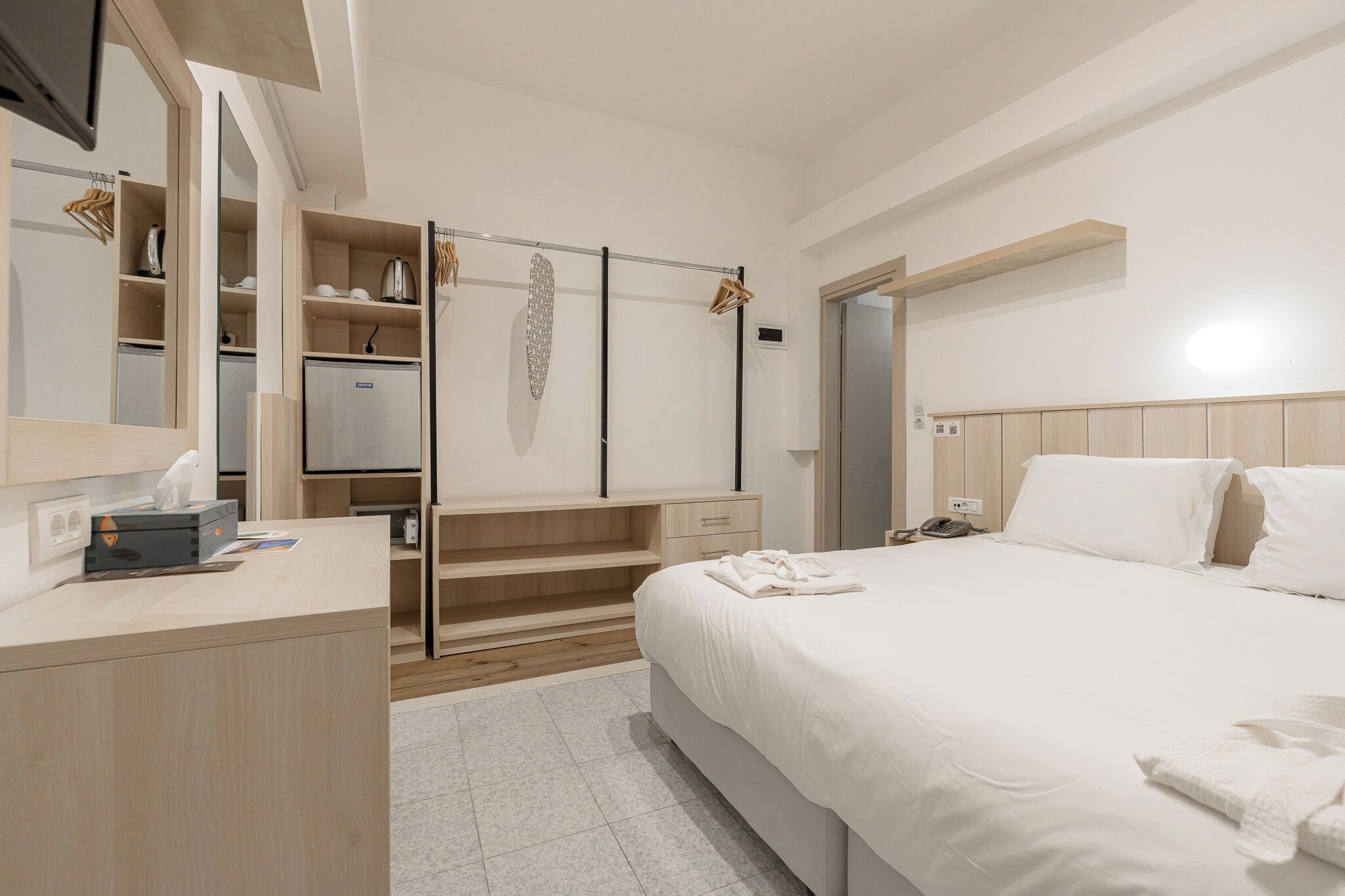 A hotel room with a bed, a desk, a wardrobe, and a mirror.