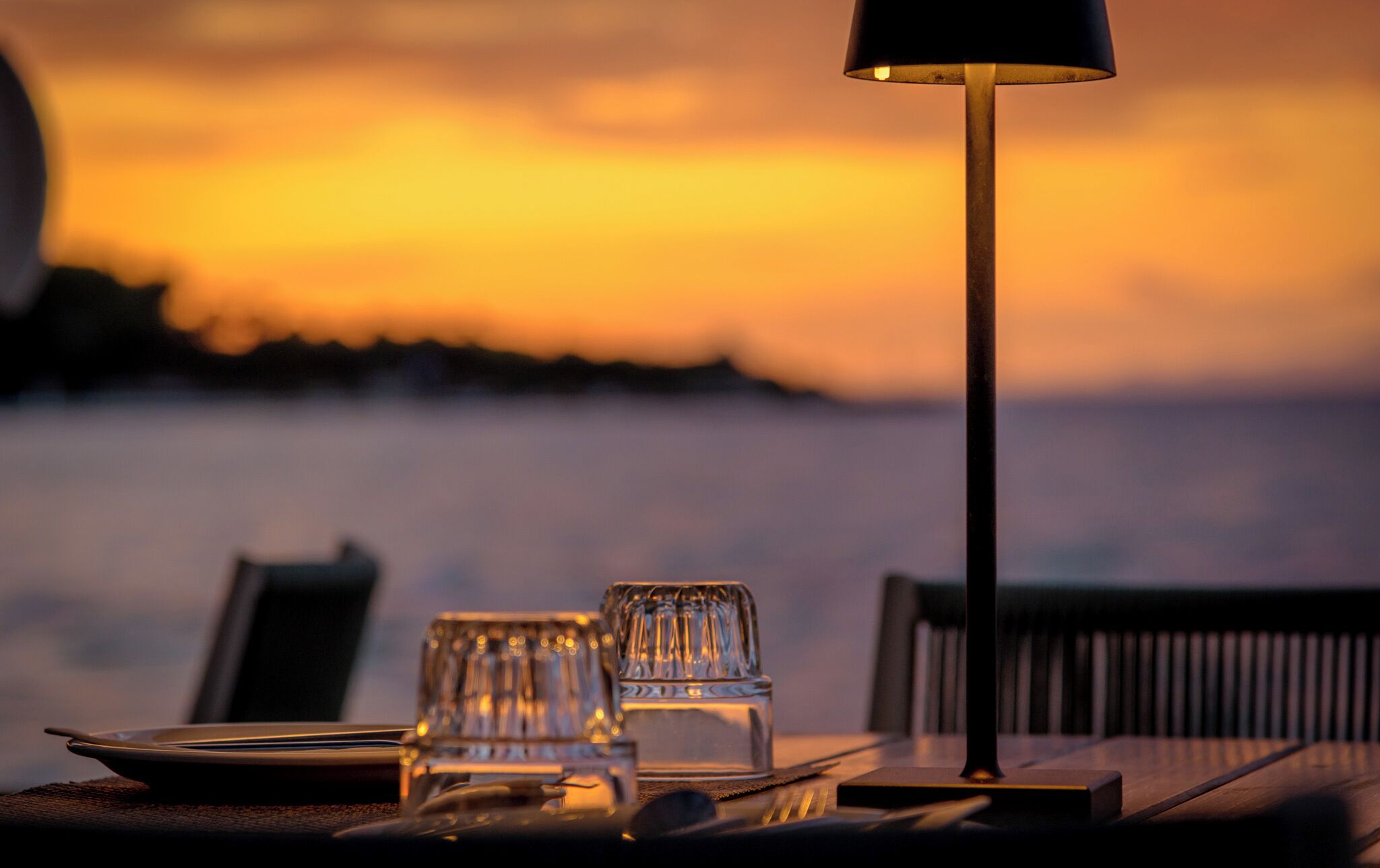A table set for two with a clear view of the sunset over the water.