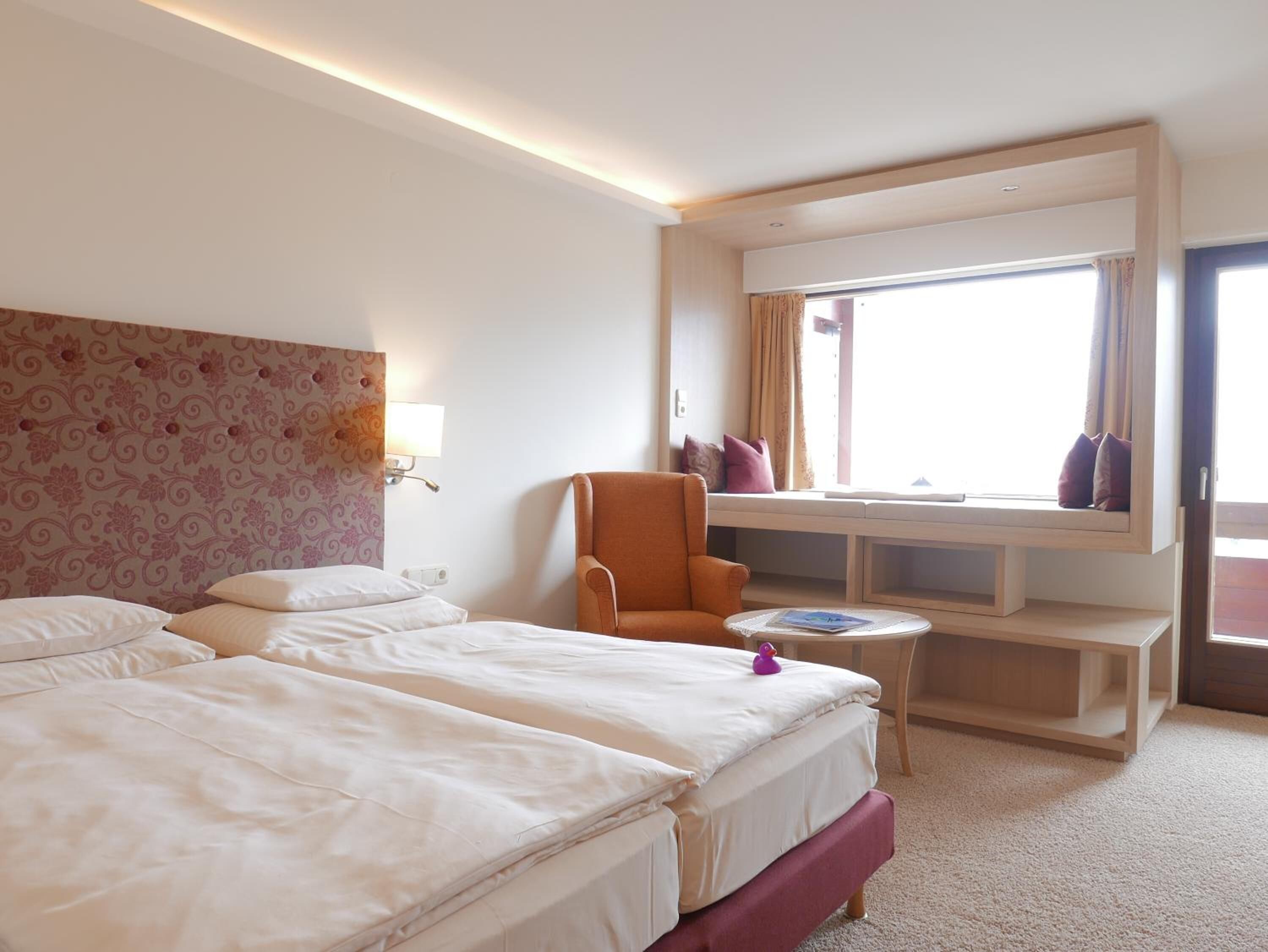 Habitación de hotel con una cama grande, una silla, una mesita y un ventanal con vistas.