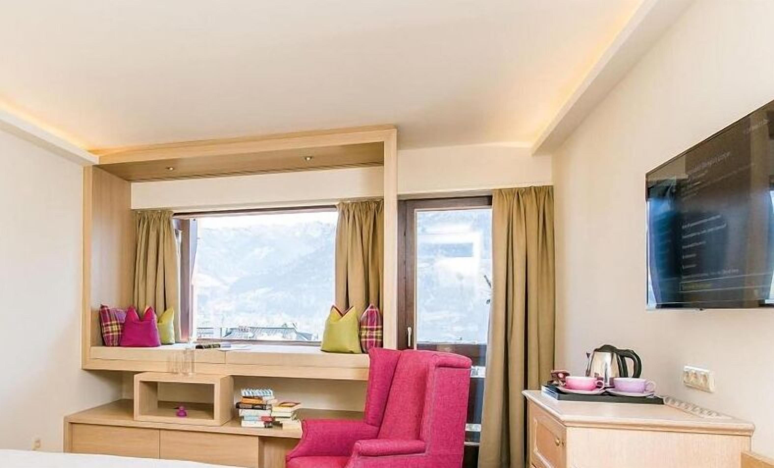 Una habitación de hotel con cama, escritorio con silla, ventana con cortinas y televisor montado en la pared.