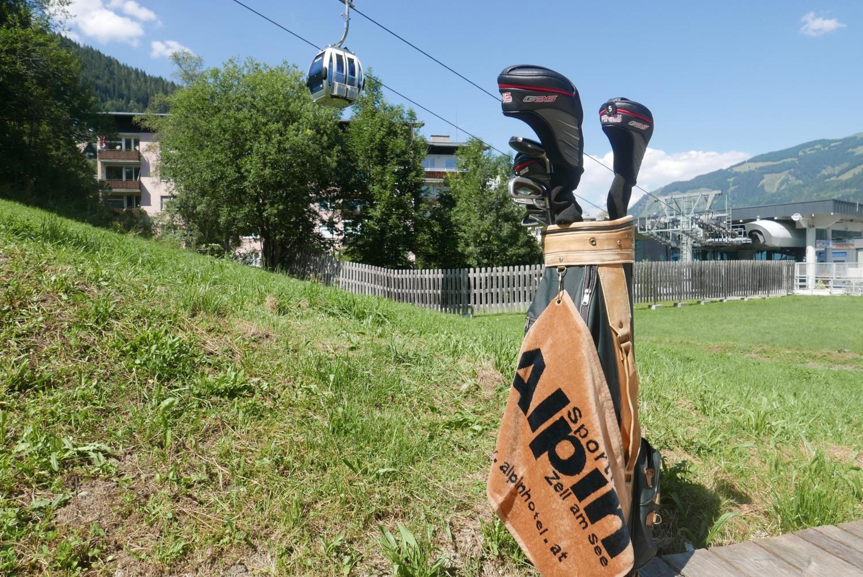 Un bolso de golf con un logotipo y texto, un teleférico al fondo y una valla de madera.