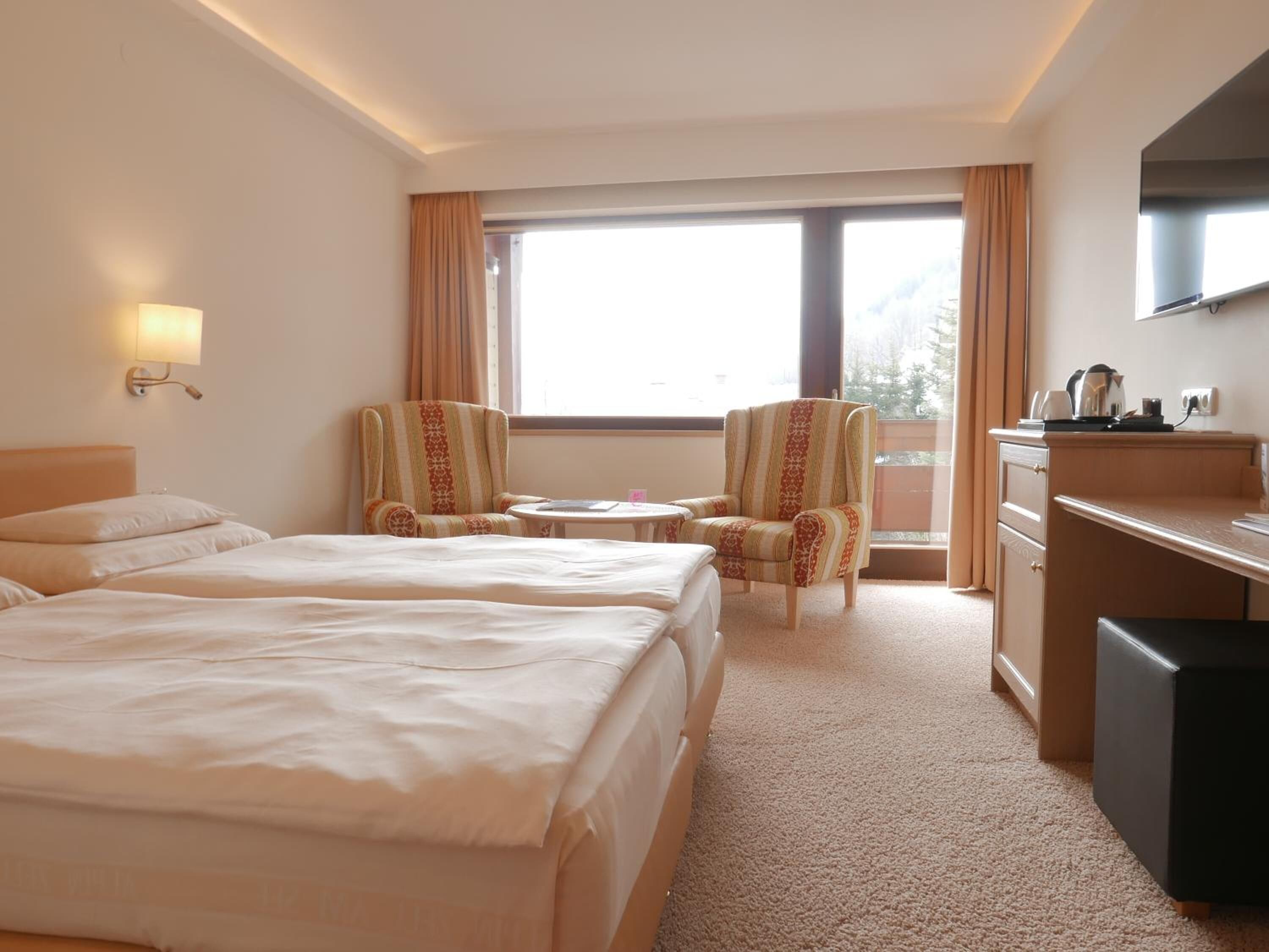 Habitación de hotel con dos camas, un escritorio con televisor, una mesita pequeña y una silla.