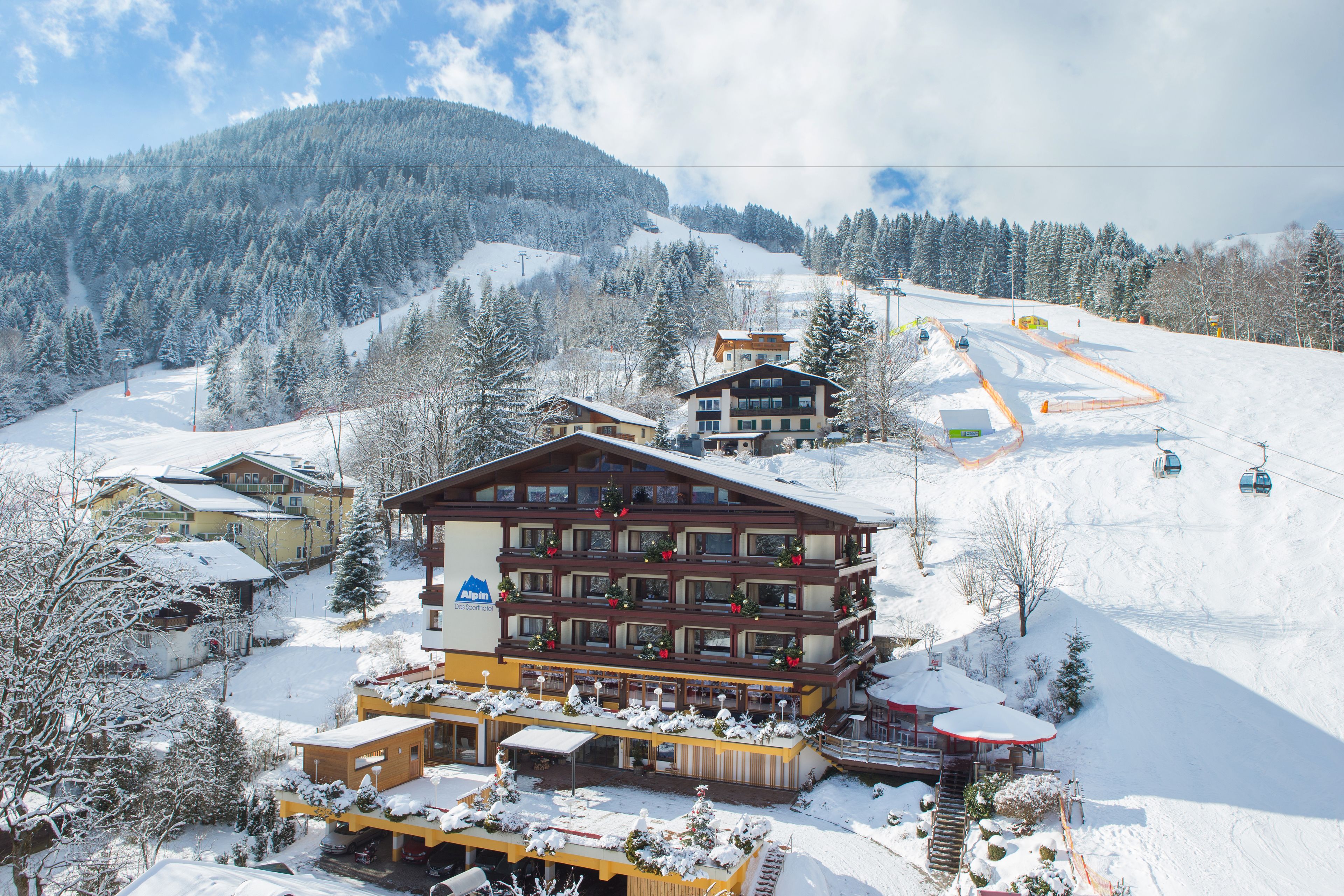 Un hotel de diversos pisos amb un remuntacamp amb fons, envoltat d'arbres coberts de neu i una muntanya.