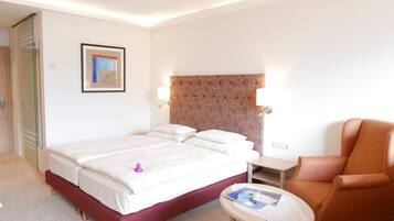 Ein Hotelzimmer mit Bett, Sessel, kleinem Tisch und einem gerahmten Bild an der Wand.
