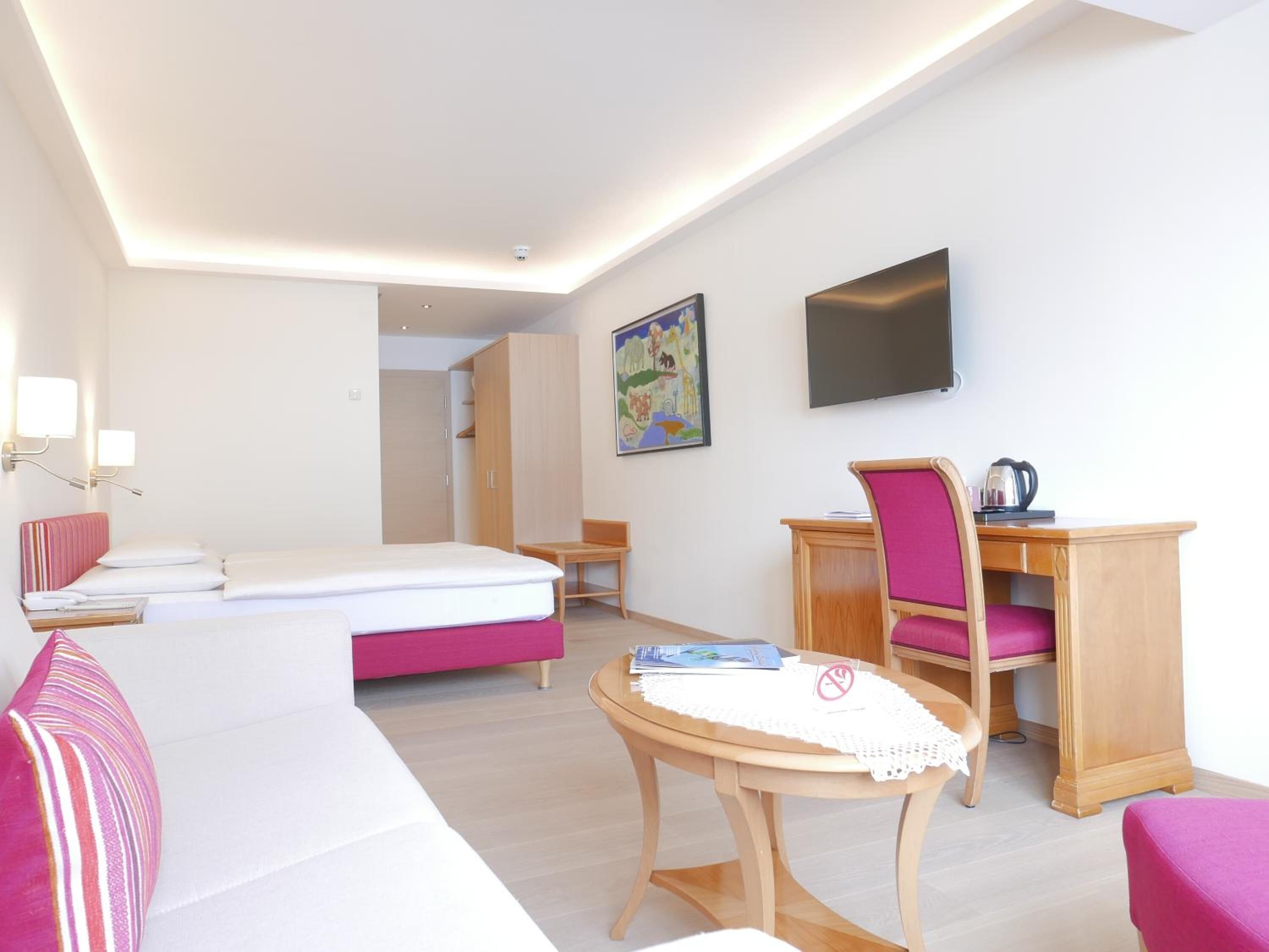 A modern hotel room with a bed, a desk, a chair, a television, and a painting on the wall.