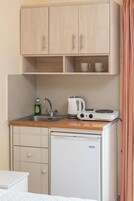 Una kitchenette compacta con un lavamanos, una tetera, un refrigerador pequeño y un mueble sobre la encimera.
