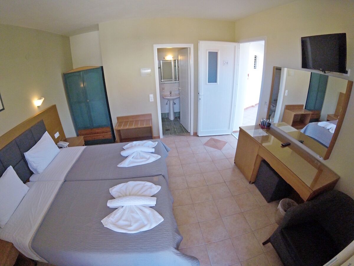 A hotel room with two beds, a desk, a chair, a TV, and a bathroom visible through an open door.