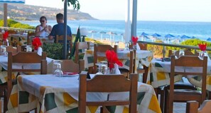 Un restaurante frente al mar con terraza, mesas dispuestas con manteles blancos y servilletas rojas.