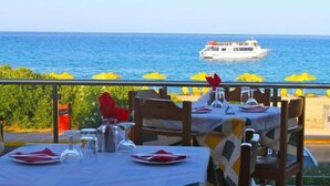 Um restaurante à beira-mar com mesas preparadas para refeições, com vista para o mar e um barco ao longe.