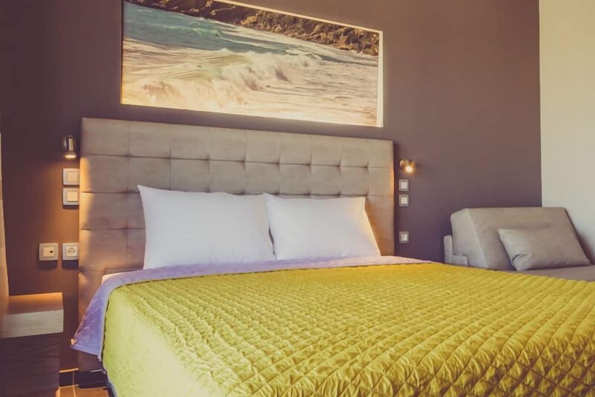 A bedroom with a large bed, a headboard, and a painting of a seascape above it.
