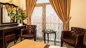 A hotel room with a bed, two leather armchairs, a small round table with a vase of flowers, a mirror, and a window with curtains. - Grand Work Hotel (Ankara)