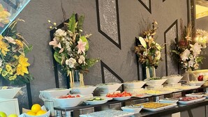 A buffet setup with various food items and decorative flowers on a counter. - Grand Work Hotel (Ankara)
