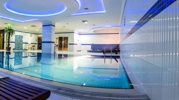 A modern indoor swimming pool with a clear water surface, surrounded by a tiled wall and a bench. - Grand Work Hotel (Ankara)