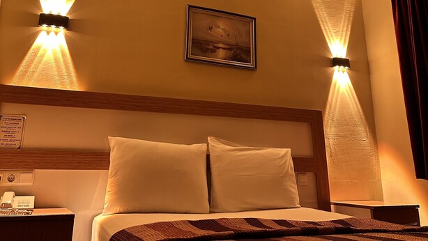 Ein Hotelzimmer mit einem Bett, zwei Wandlampen, einem gerahmten Bild und einem Nachttisch mit Telefon.