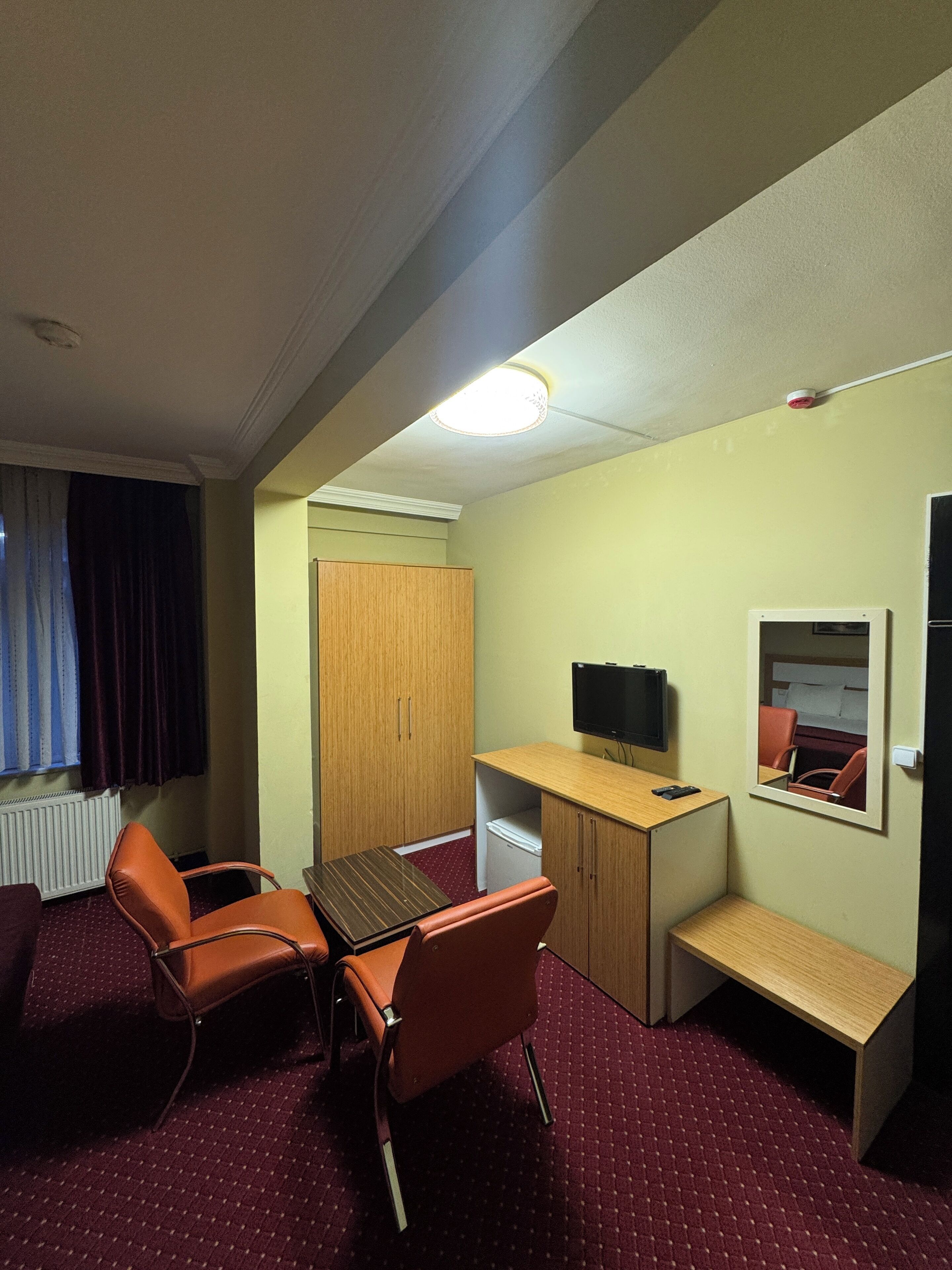 Una habitación de hotel con escritorio, dos sillas, televisor, espejo y armario.