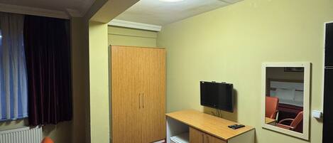 Una habitación de hotel con escritorio, dos sillas, televisor, espejo y armario.