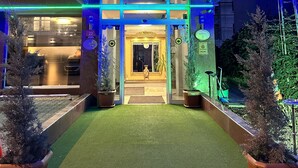 Die Fassade des Mina Hotels mit beleuchteter Beschilderung, einem zentralen Eingang und Blumentöpfen im Vordergrund.