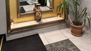 Ein großer, verzierter Spiegel mit goldener Rahmung, eine Topfpflanze und eine kleine Vase auf einem Fliesenboden.