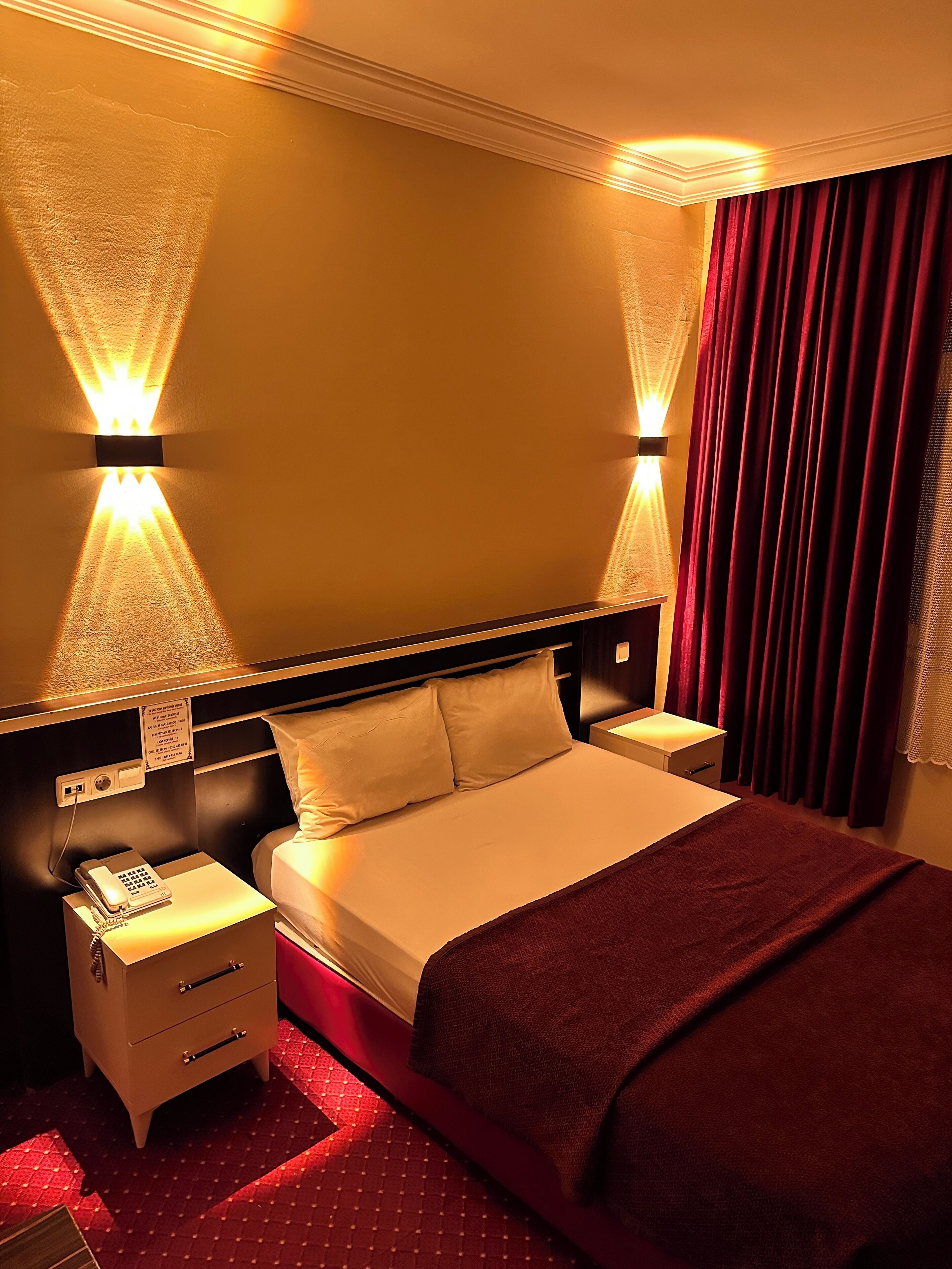 Een hotelkamer met een groot bed, twee nachtkastjes, een telefoon en een bord aan de muur.
