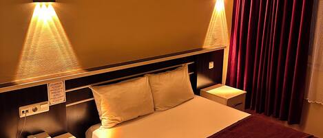 Een hotelkamer met een groot bed, twee nachtkastjes, een telefoon en een bord aan de muur.