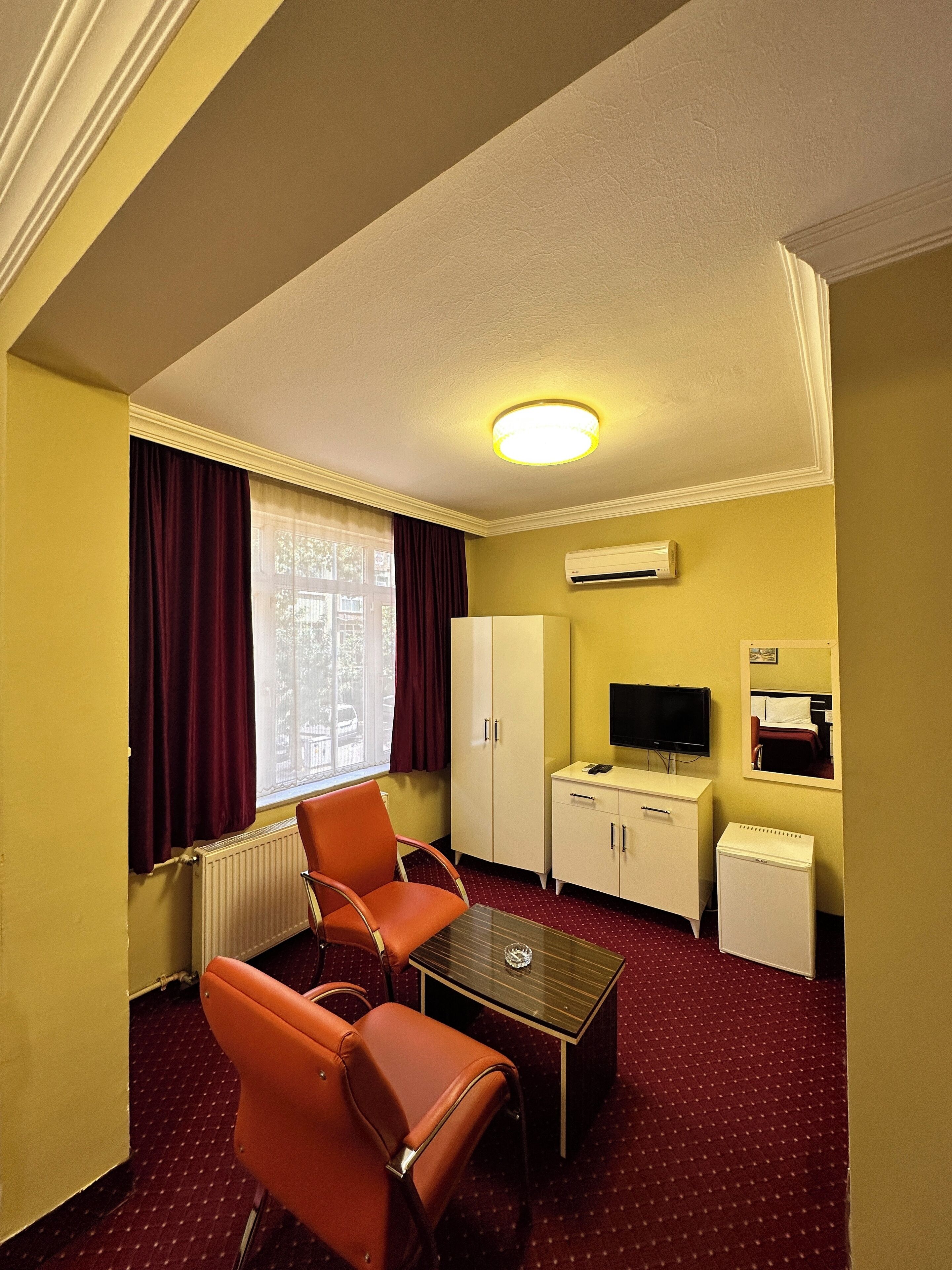 Een hotelkamer met een tafel, twee stoelen, een televisie, een kledingkast en een airconditioner.