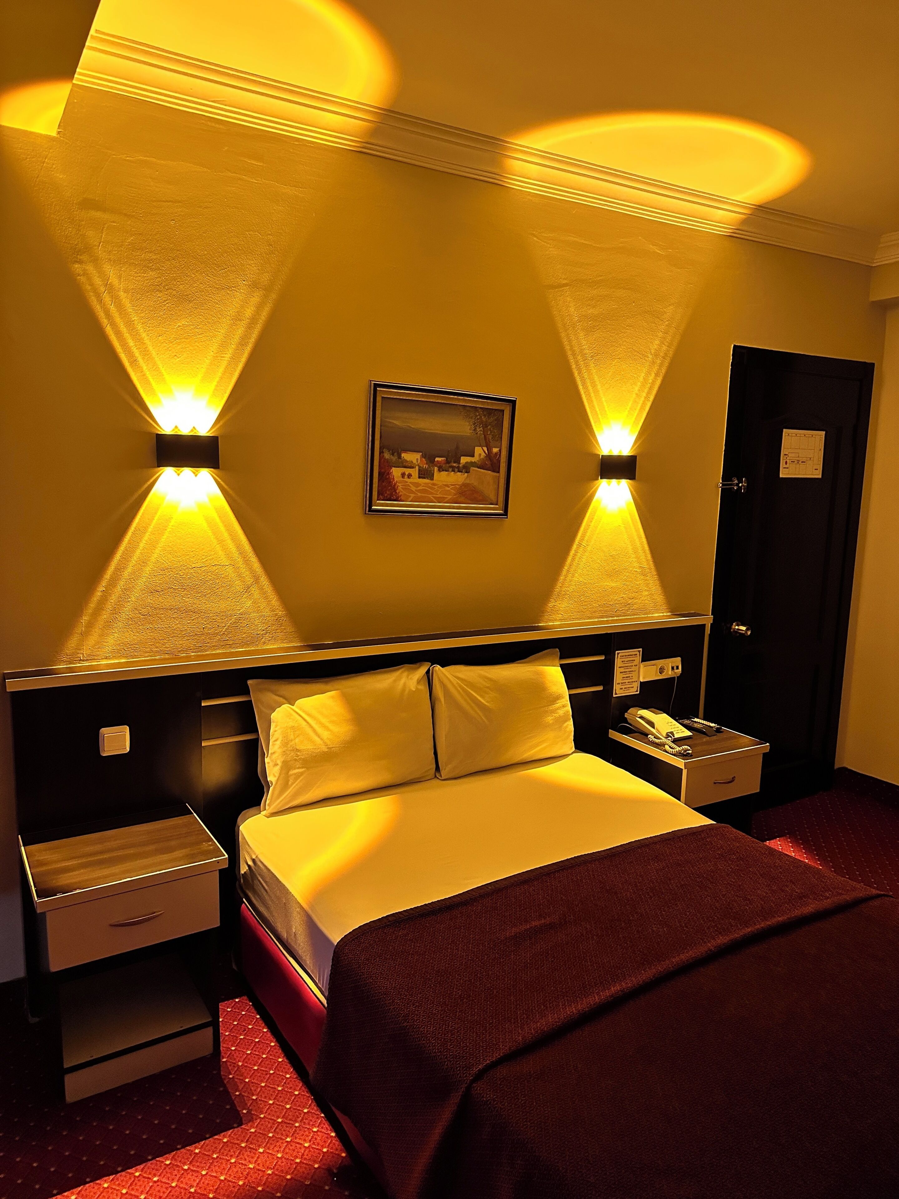 A hotel room with a bed, bedside tables, a nightstand, a telephone, and a door.