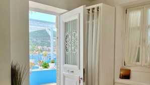 Habitació d'hotel amb un llit, una petita taula de nit, una finestra amb cortines, vista d'un pont i una vila costanera, i una porta que dona a una zona exterior.