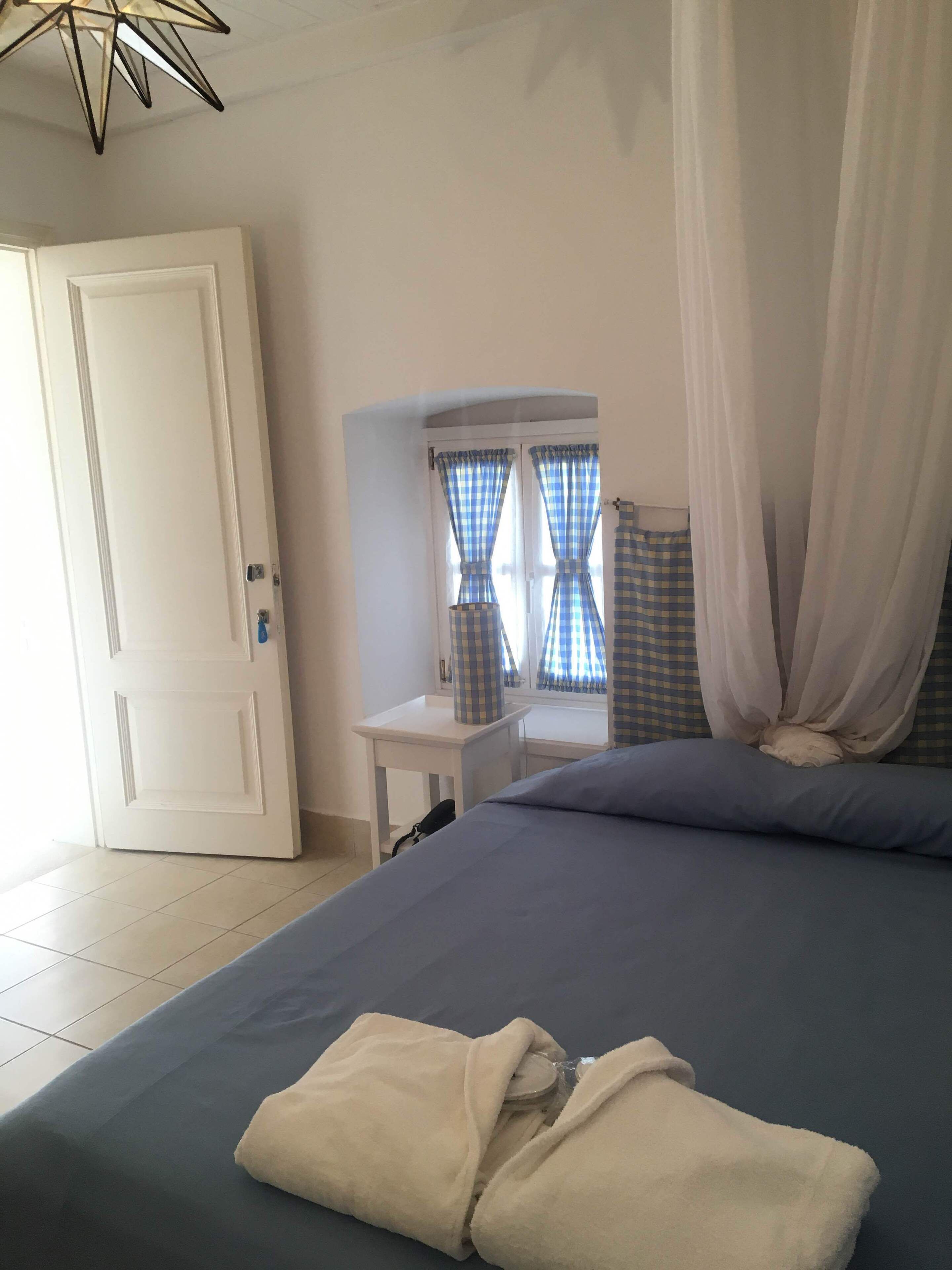 A bedroom with a bed, a bedside table, a window with curtains, and a door.