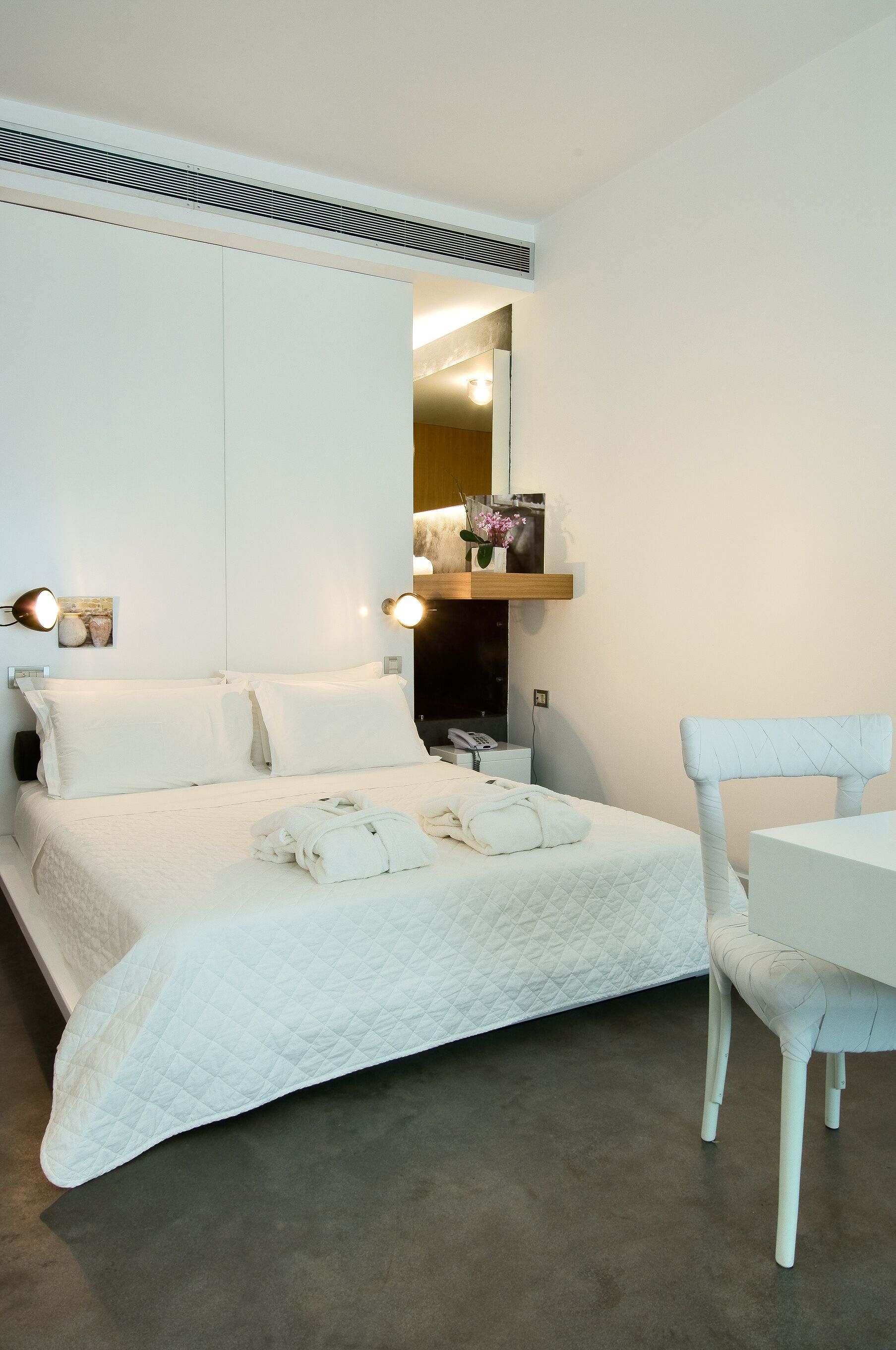 Un dormitorio con cama, mesita de noche, silla y espejo.