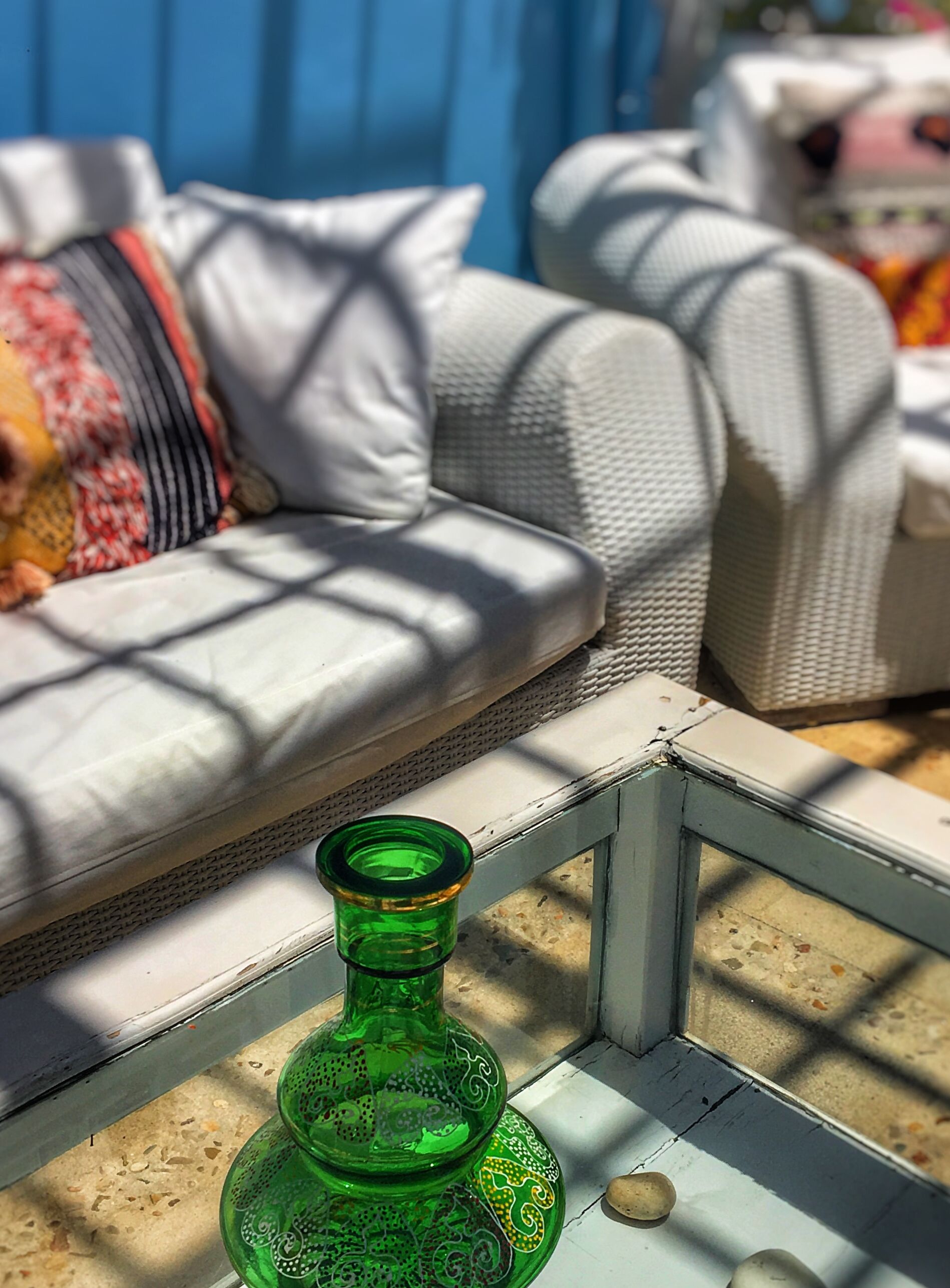 Een groene glazen fles op een tafel met een witte lijst, een grijze bank met gekleurde kussens, en een blauwe achtergrond.