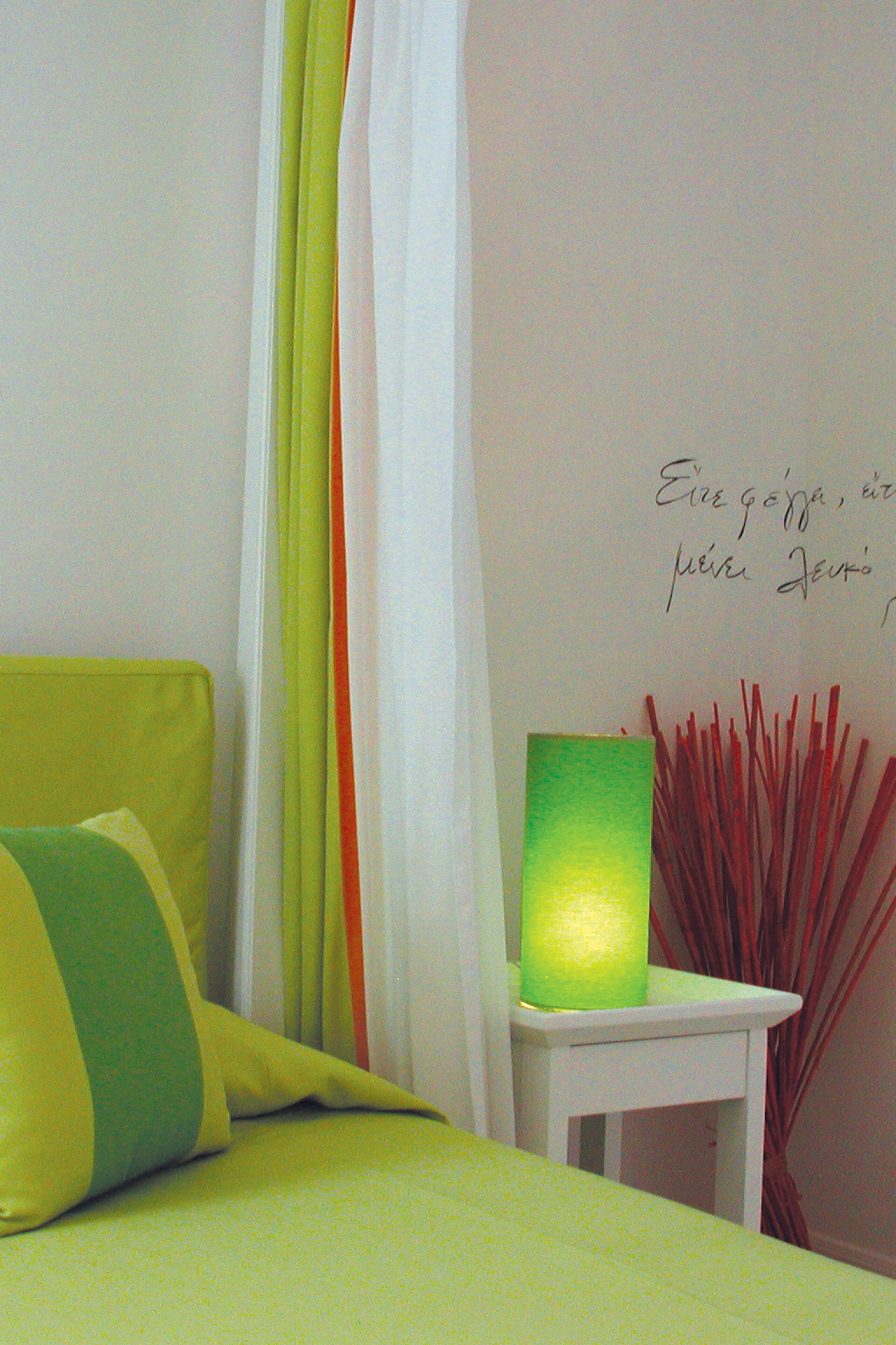 Een bed met groene beddengoed, een witte nachtkastje met een groene lamp en een muur met rode decoratieve elementen.