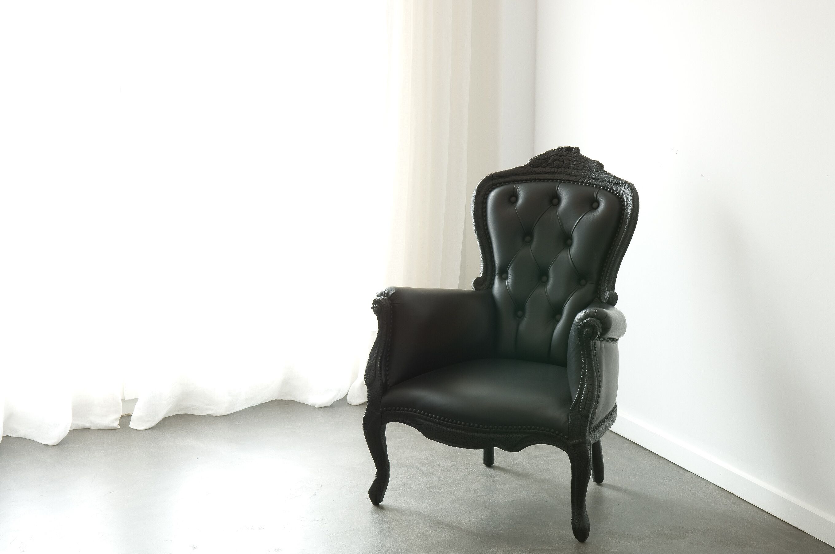 Un sillón tapizado de verde oscuro con respaldo capitonado y patas curvadas, ubicado en una habitación con pared blanca lisa y piso de color claro.