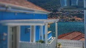Un edifici costaner amb façana blava, un balcó i vista al mar i a les muntanyes de fons.