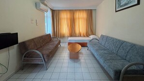Ein Wohnzimmer mit zwei Sofas, einem Couchtisch, einem Fernseher und einem Bett mit Vorhängen.