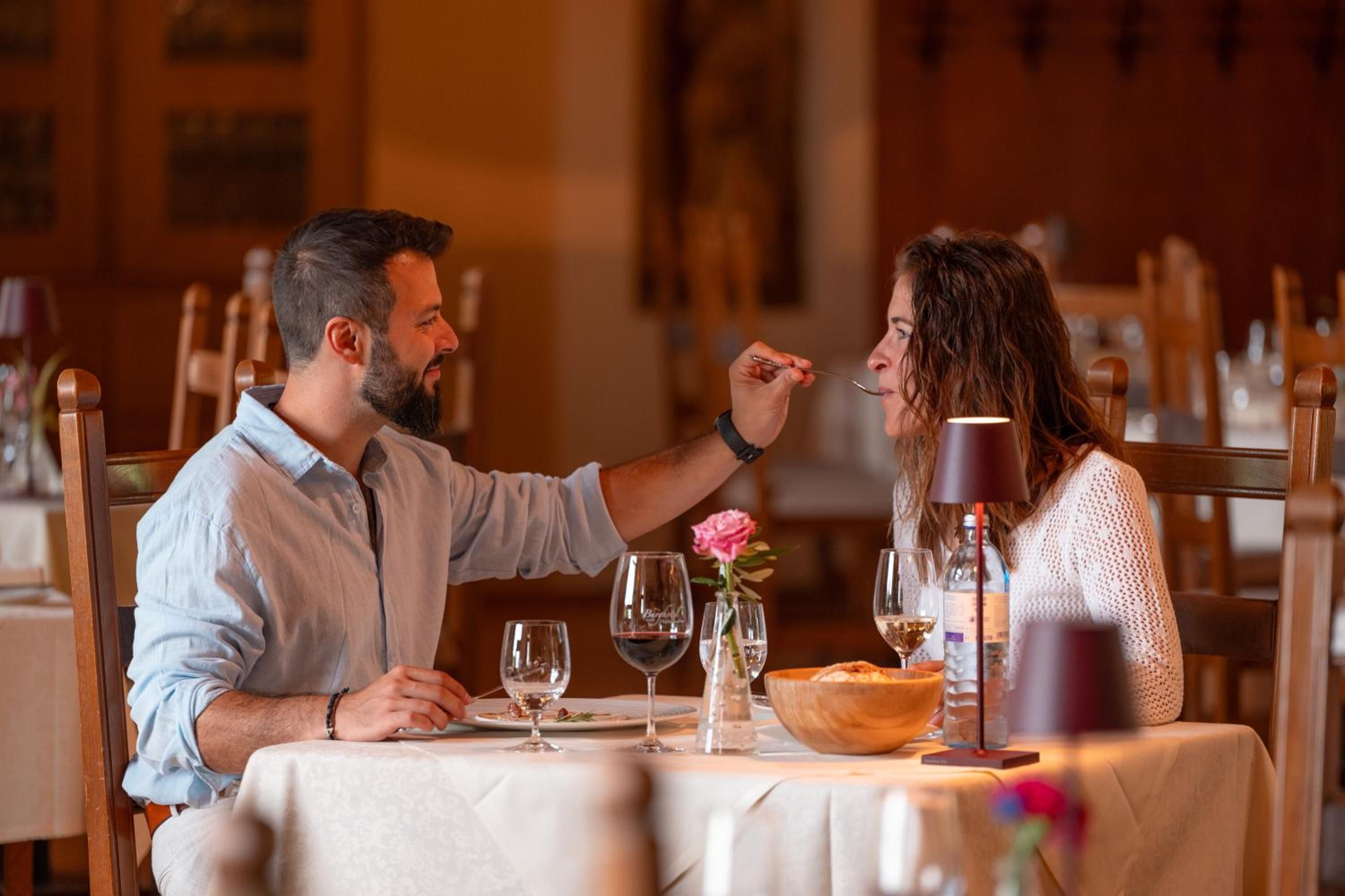 A couple dining at a table with wine glasses, a water bottle, and a flower vase.