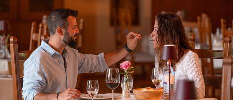 A couple dining at a table with wine glasses, a water bottle, and a flower vase.