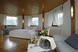 A hotel room with a bed, a sofa, a table with a bottle of champagne, glasses, and fruit.