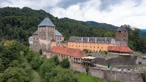 Un castillo histórico con torres de piedra, un amplio patio interior y un paisaje boscoso circundante.