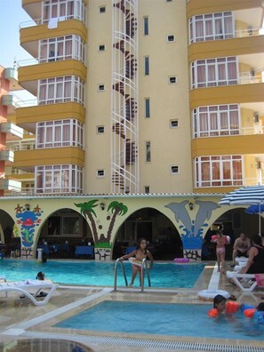 Ett hotell med ett poolområde som inkluderar en vattenrutschkana, solstolar och en väggmålning med palmer och delfiner.