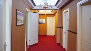 A hotel hallway with a red carpet, white doors, and a chandelier. - Aegean Sea Rooms (Chios City)