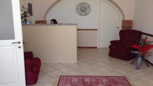A reception area with a desk, a red armchair, a clock on the wall, and a tiled floor. - Aegean Sea Rooms (Chios City)