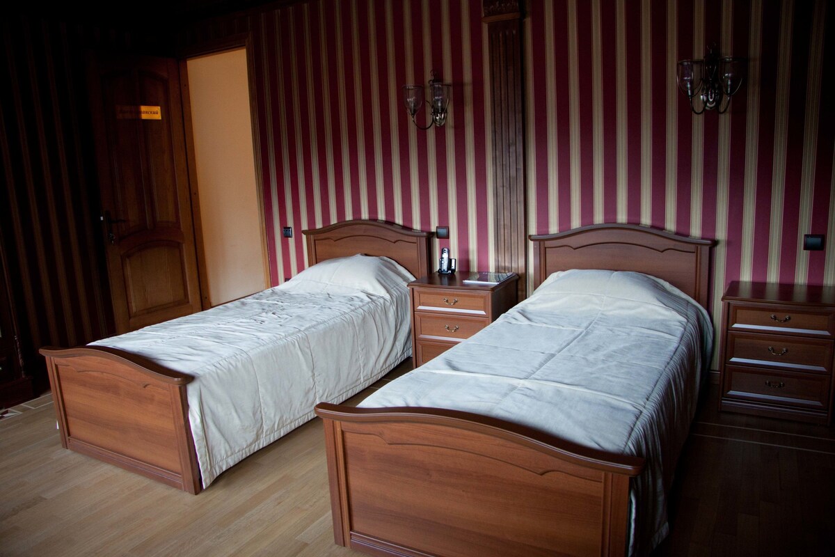 Une chambre avec deux lits en bois, une armoire en bois, une table de chevet et un miroir.